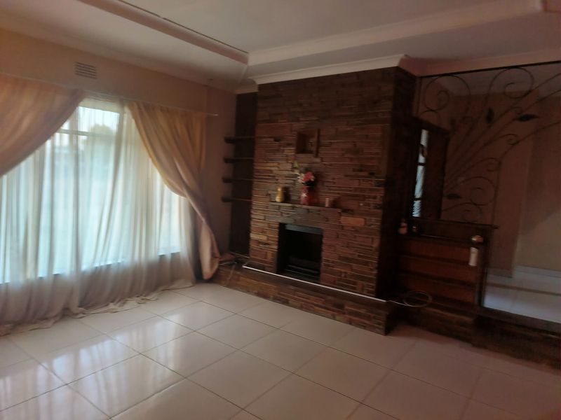 Spacious living room featuring a prominent stone-clad fireplace, tiled flooring, and decorative wrought iron detailing, offering a solid foundation for modern updates.