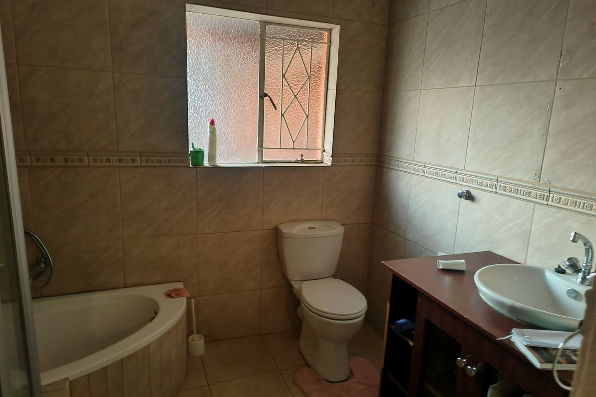A functional bathroom featuring a corner bathtub, vanity with vessel sink, and full-height wall tiling.