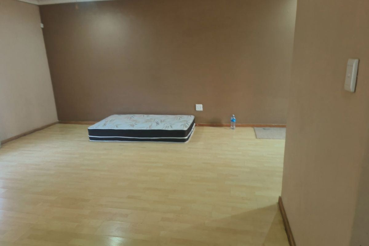 A spacious, empty bedroom featuring light-toned laminate flooring and neutral-colored walls, providing a blank canvas for personalization.