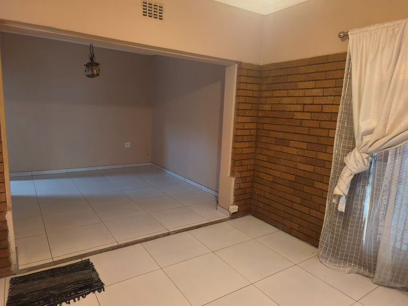 An open-plan living area featuring ceramic floor tiles and a prominent exposed brick feature wall, offering a versatile space for interior design.