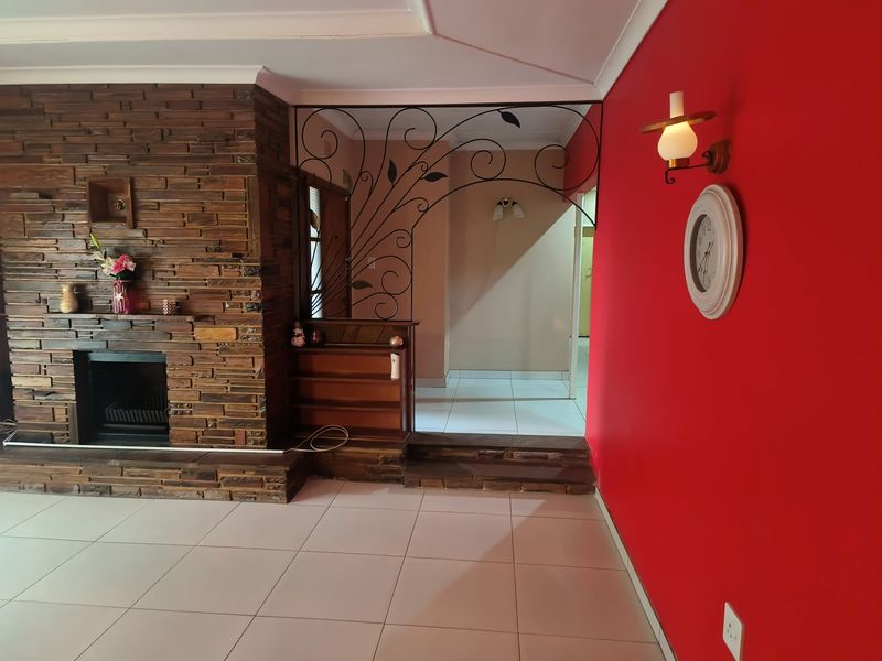 Living area featuring a prominent stone-clad fireplace, decorative wrought iron room divider, and tiled flooring with a raised transition to the hallway.