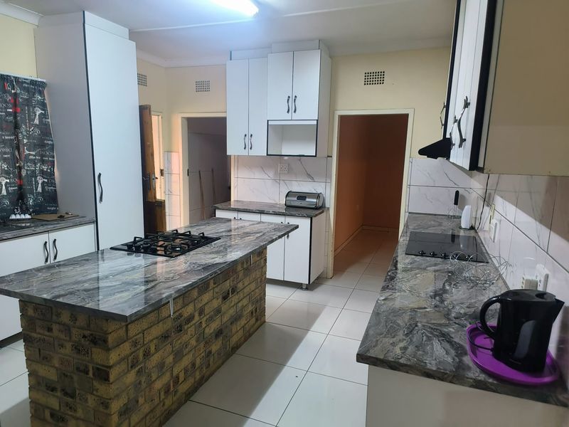 A functional kitchen featuring a central brick-based island with a gas hob, marble-effect countertops, white cabinetry, and tiled flooring.