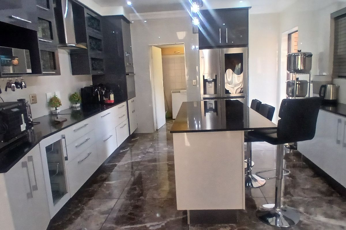 Modern kitchen featuring high-gloss cabinetry, a central island with breakfast bar seating, dark granite countertops, and polished tiled flooring.
