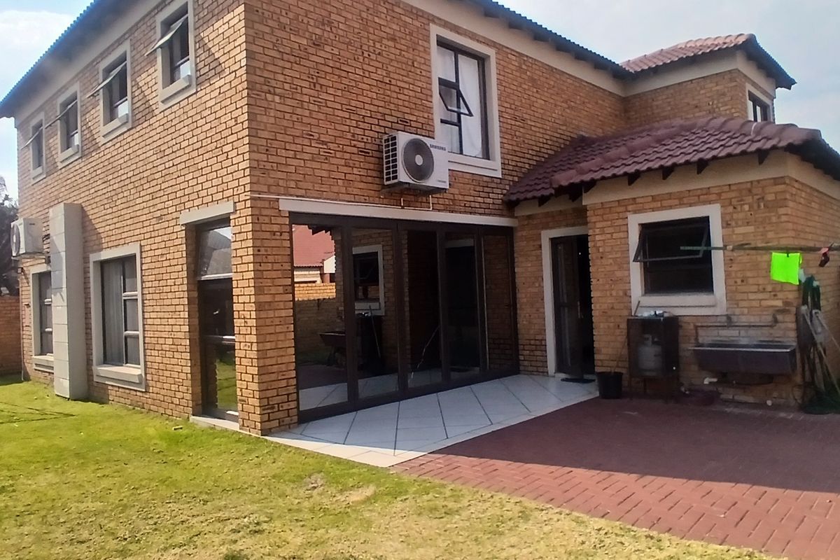 Rear view of a double-storey facebrick cluster home featuring a paved patio, external wash basin, and a private garden area.