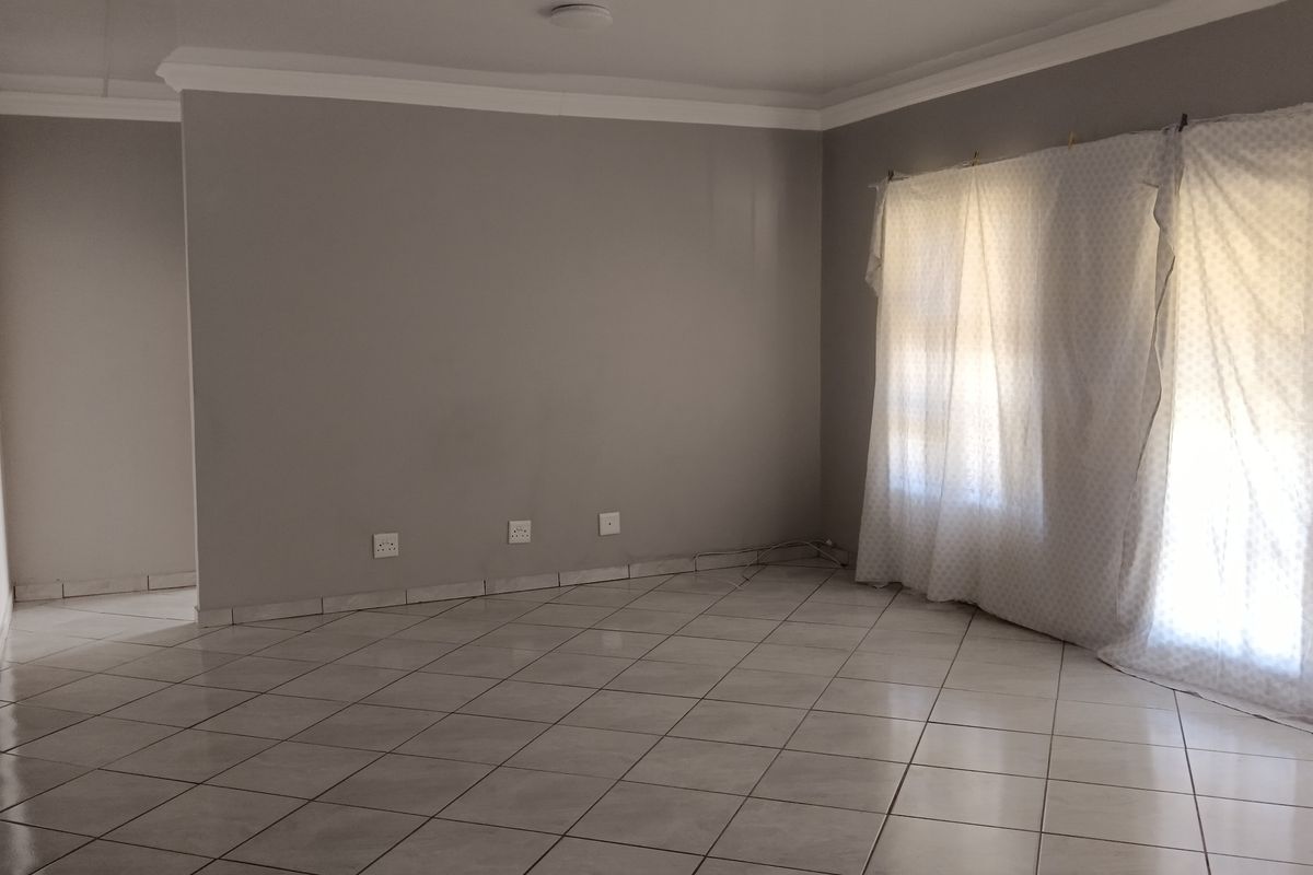 A spacious, empty living area featuring neutral grey walls, tiled flooring, and classic cove cornicing, providing a blank canvas for interior design.