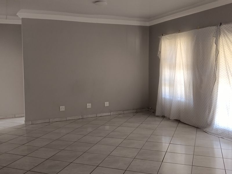 A spacious, empty living area featuring neutral grey walls, tiled flooring, and classic cove cornicing, providing a blank canvas for interior design.