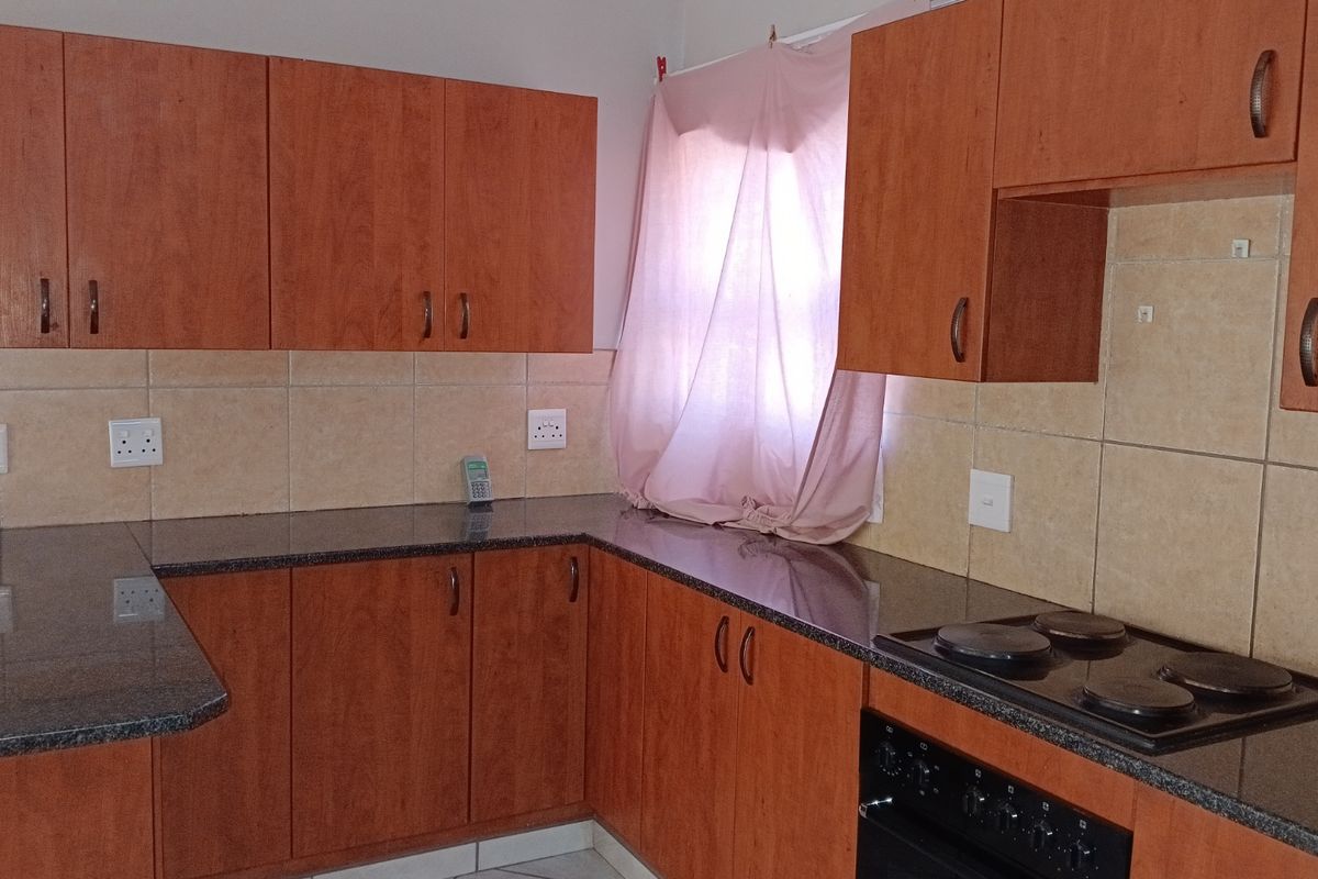A functional kitchen featuring wood-look laminate cabinetry, granite countertops, a tiled backsplash, and a built-in electric oven and hob.