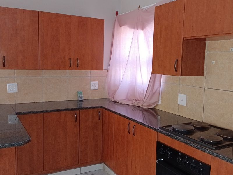 A functional kitchen featuring wood-look laminate cabinetry, granite countertops, a tiled backsplash, and a built-in electric oven and hob.