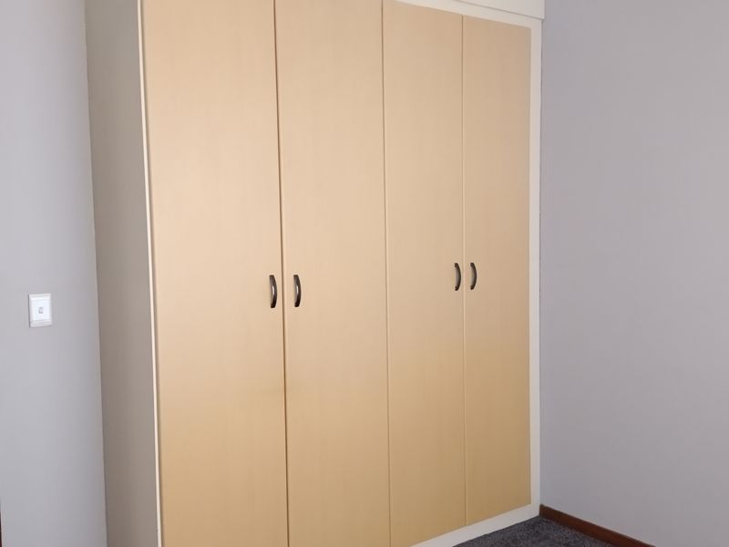 A bedroom featuring a large, light-wood built-in wardrobe with four doors, neutral wall paint, and dark carpeting.