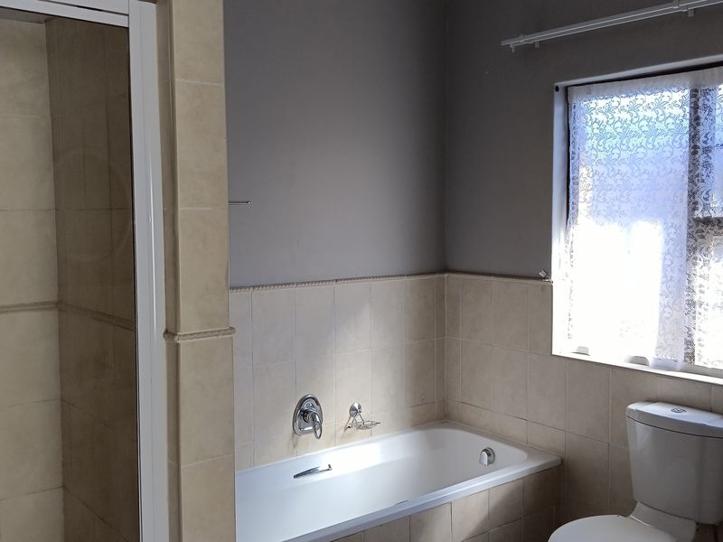A functional bathroom featuring a built-in bathtub, separate shower enclosure, and neutral wall tiling, offering a clean and practical layout.
