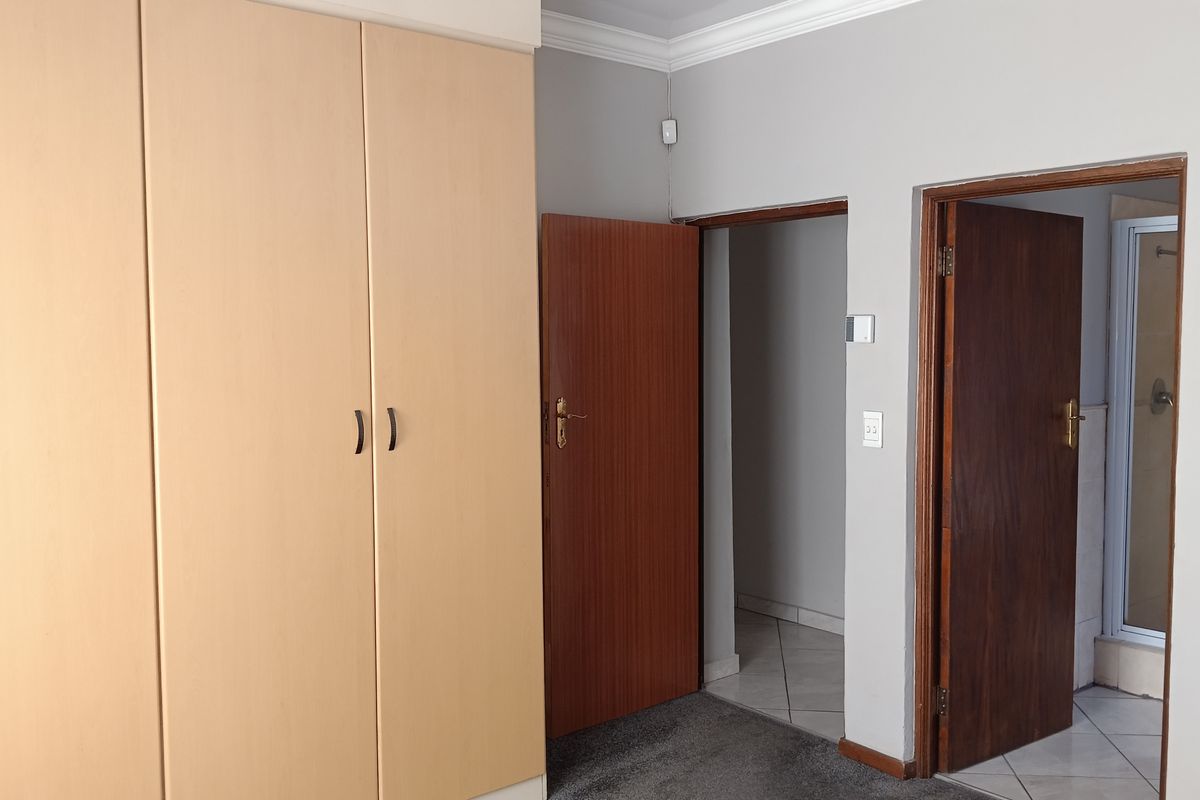 A bedroom featuring built-in cupboards, carpeted flooring, and direct access to an en-suite bathroom with tiled flooring.