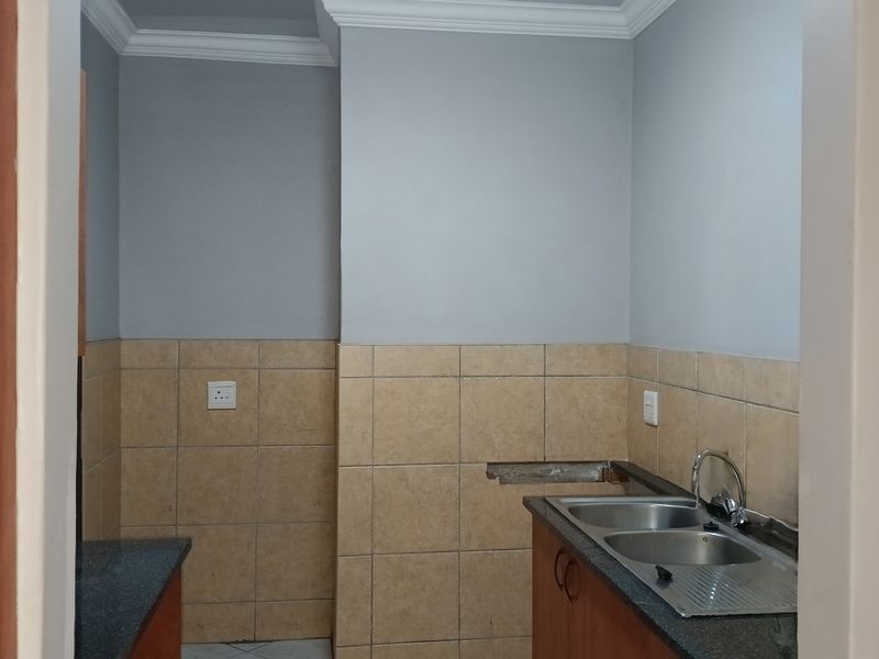 A functional scullery area featuring a double bowl stainless steel sink, granite countertops, and tiled splashbacks, requiring minor repairs to the wall finish.