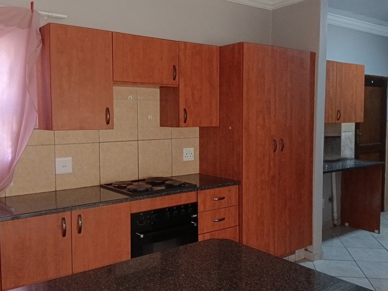 A functional kitchen featuring wood-look cabinetry, dark laminate countertops, an integrated electric hob and oven, and tiled backsplash and flooring.
