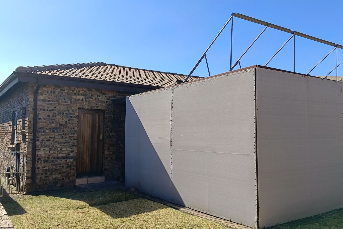 Rear view of a face brick house featuring a tiled roof and an unfinished metal frame structure with a canvas enclosure.