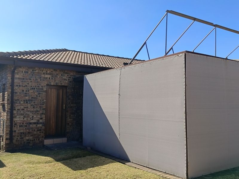 Rear view of a face brick house featuring a tiled roof and an unfinished metal frame structure with a canvas enclosure.