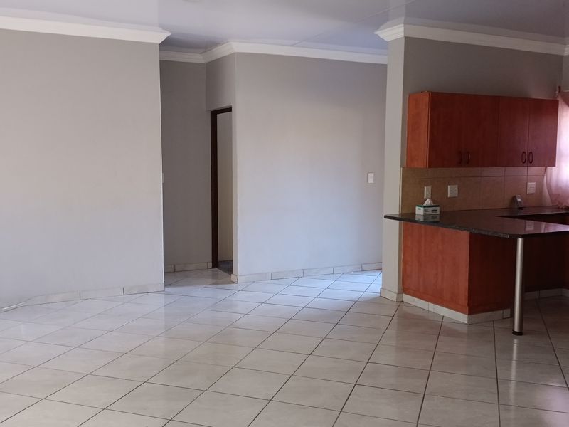An open-plan living and kitchen area featuring neutral walls, tiled flooring, and wooden cabinetry with granite countertops.