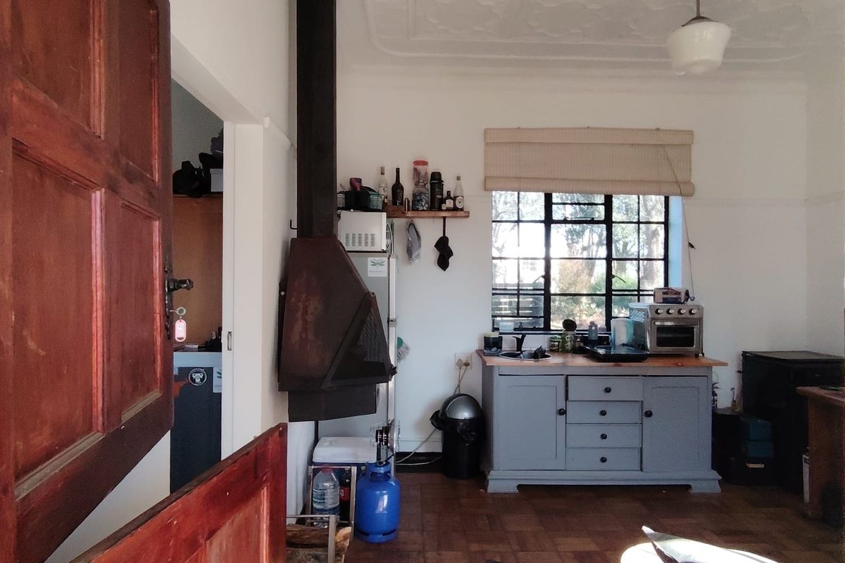 A rustic kitchen area featuring original parquet flooring, a decorative pressed metal ceiling, and a prominent wood-burning fireplace with a steel-framed window.