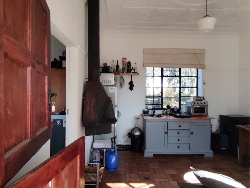 A rustic kitchen area featuring original parquet flooring, a decorative pressed metal ceiling, and a prominent wood-burning fireplace with a steel-framed window.