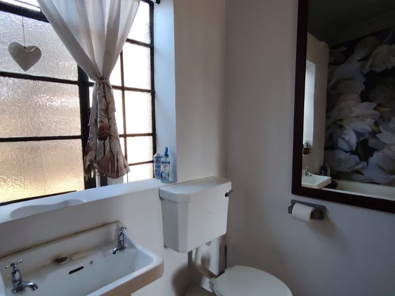 A compact bathroom featuring a wall-mounted basin, a toilet with a high-level cistern, and a large framed mirror.