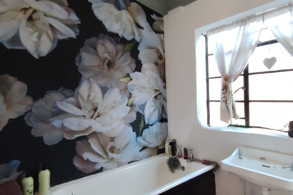 A bathroom featuring a bathtub, wall-mounted basin, and a distinctive floral feature wall, complemented by a steel-framed window.