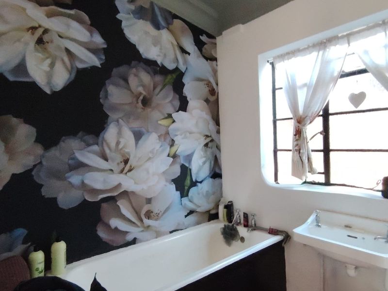 A bathroom featuring a bathtub, wall-mounted basin, and a distinctive floral feature wall, complemented by a steel-framed window.