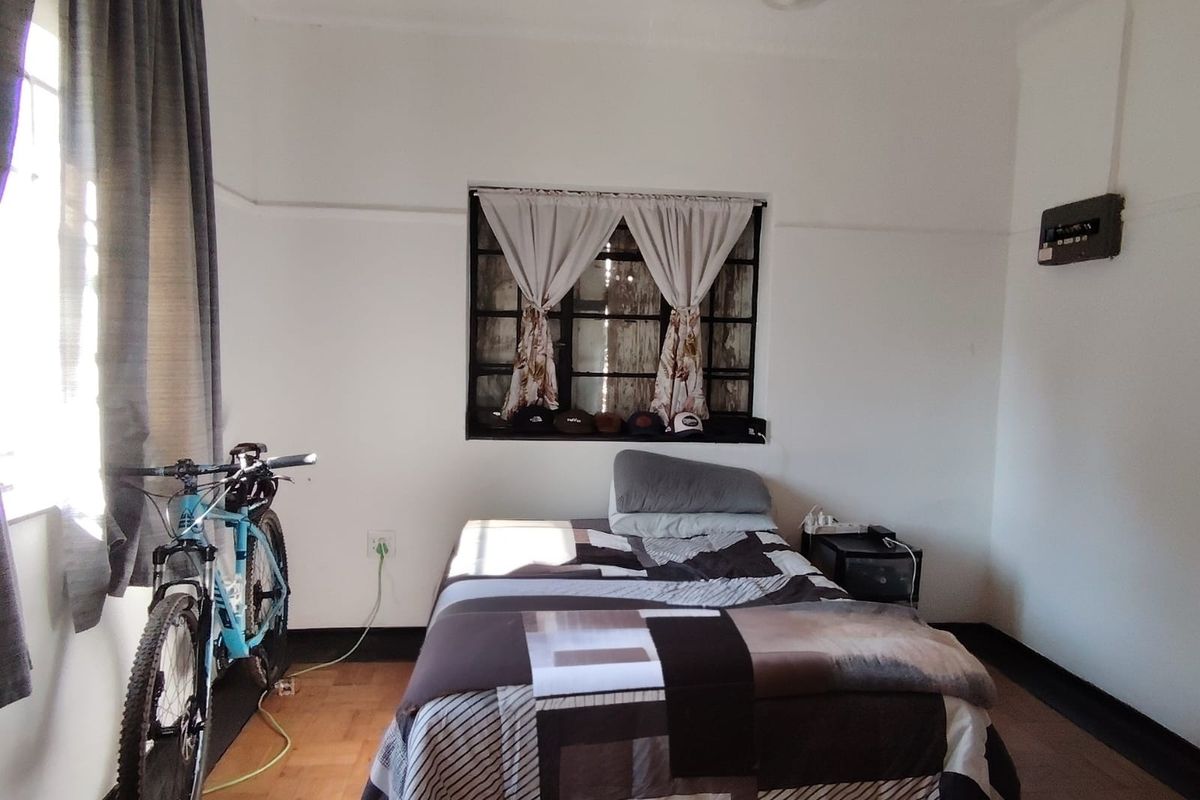 A bedroom featuring original parquet flooring, an ornate ceiling, and a steel-framed window, offering a classic cottage aesthetic with potential for modernization.