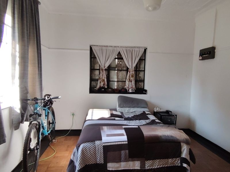 A bedroom featuring original parquet flooring, an ornate ceiling, and a steel-framed window, offering a classic cottage aesthetic with potential for modernization.