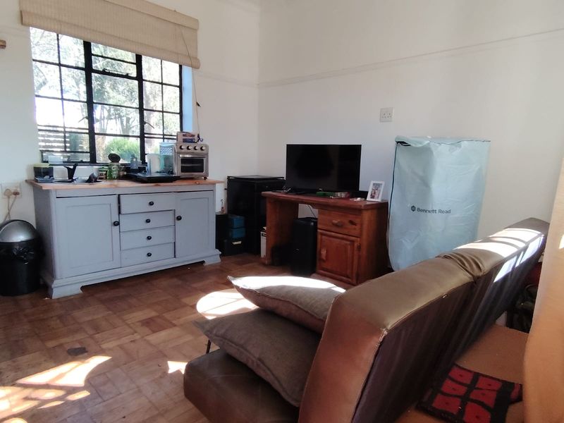 A living room featuring original parquet flooring, ornate ceiling cornices, and a steel-framed window, offering a classic cottage aesthetic with potential for modernization.