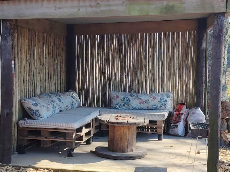 A rustic outdoor covered patio area featuring a timber-framed structure with natural wood slat wall cladding and a concrete floor.