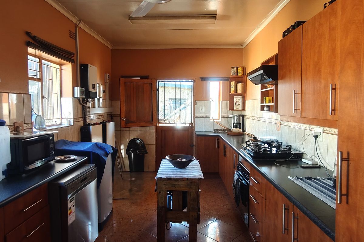 A functional kitchen featuring wooden cabinetry, dark countertops, a gas hob with extractor fan, and tiled flooring with direct access to the exterior.