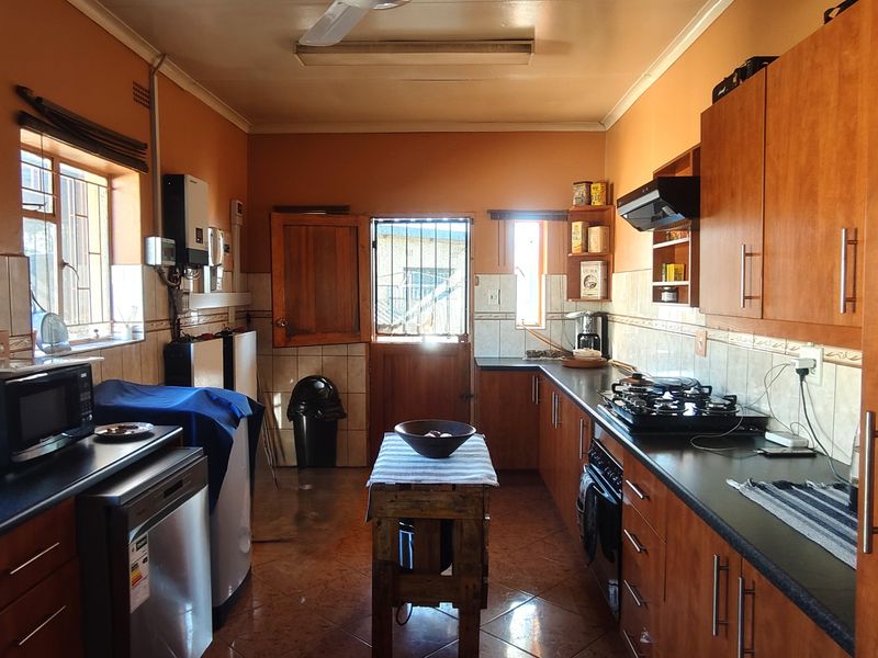 A functional kitchen featuring wooden cabinetry, dark countertops, a gas hob with extractor fan, and tiled flooring with direct access to the exterior.
