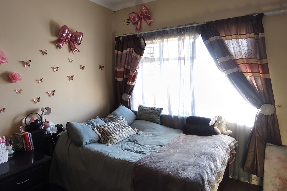 A bedroom featuring a window with security bars and a curtain rod, providing natural light to the space.