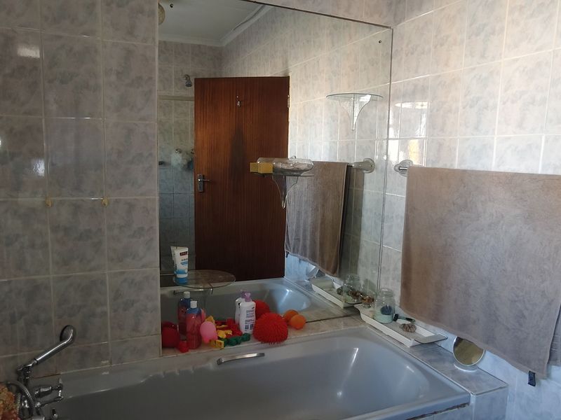 A functional bathroom featuring a built-in bathtub, large wall mirror, and full-height ceramic wall tiling.