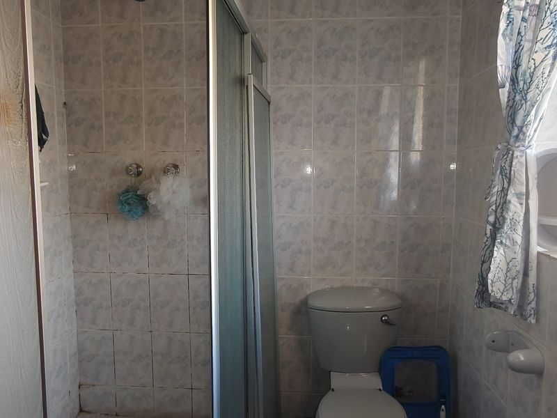 A functional bathroom featuring a shower enclosure, toilet, and tiled wall finishes, offering potential for modernization and cosmetic updates.
