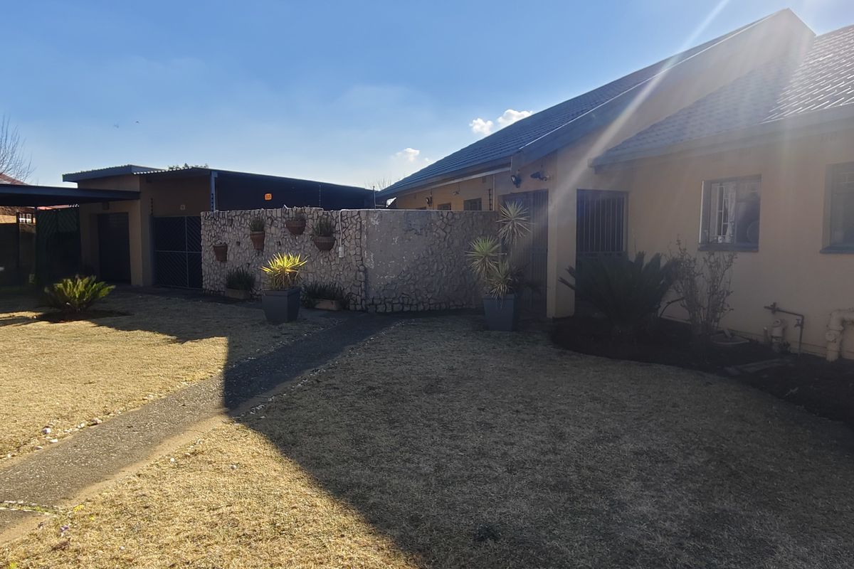 Rear exterior view of the property featuring a tiled roof, stone-clad boundary wall, paved walkway, and established garden area.