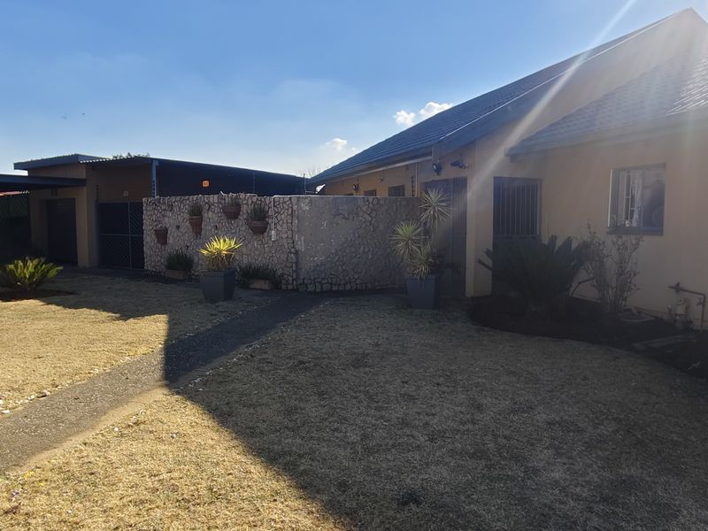 Rear exterior view of the property featuring a tiled roof, stone-clad boundary wall, paved walkway, and established garden area.