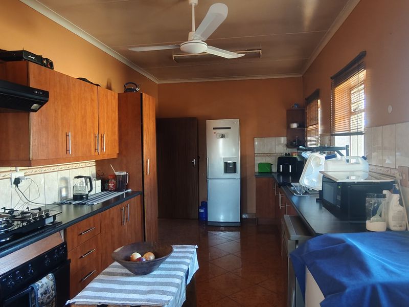 A functional kitchen featuring wooden cabinetry, a gas hob with extractor fan, tiled splashbacks, and tiled flooring, offering a practical layout for daily use.