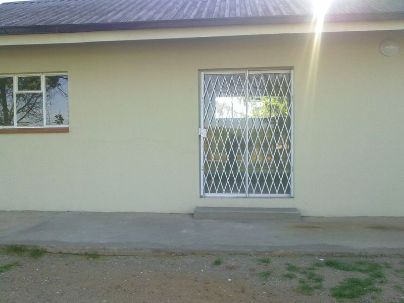 Rear exterior view of the property featuring a concrete patio, security gate, and metal-framed window.