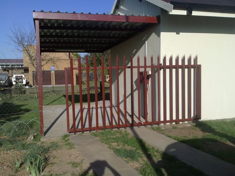 Exterior view of the property featuring a covered carport, metal security gate, and concrete driveway access.