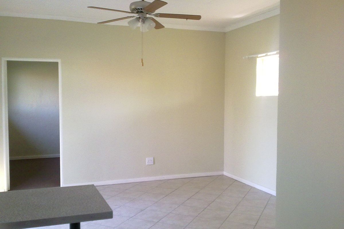 An empty living area featuring neutral tiled flooring, a ceiling fan, and coved cornicing, offering a blank canvas for interior design.