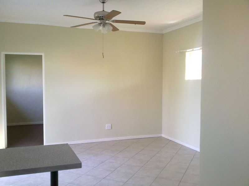 An empty living area featuring neutral tiled flooring, a ceiling fan, and coved cornicing, offering a blank canvas for interior design.