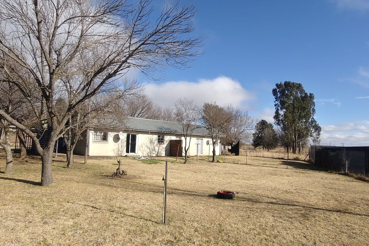 A wide-angle view of the rear exterior of the house, featuring a large open yard, metal roofing, and perimeter fencing.
