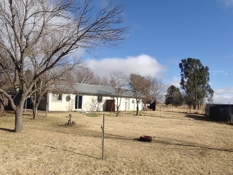 A wide-angle view of the rear exterior of the house, featuring a large open yard, metal roofing, and perimeter fencing.