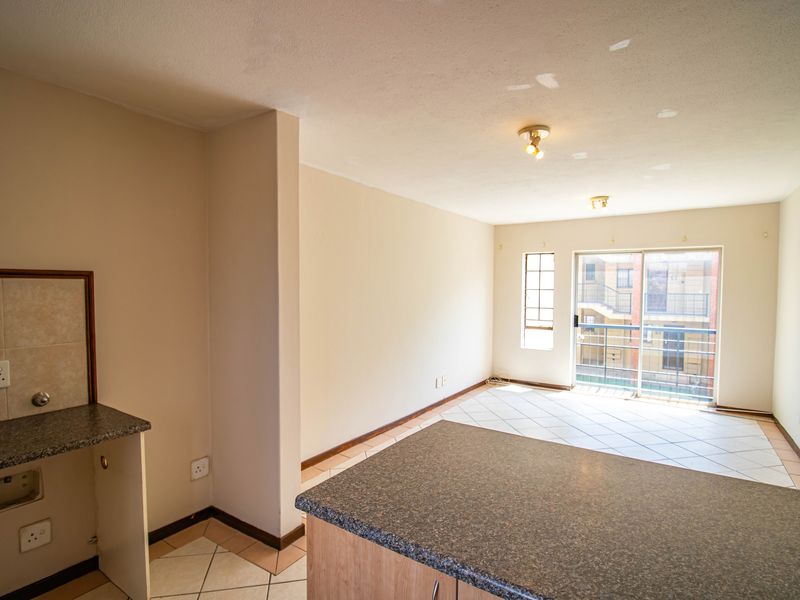 An open-plan living and kitchen area featuring tiled floors, a granite breakfast counter, and sliding door access to a balcony.