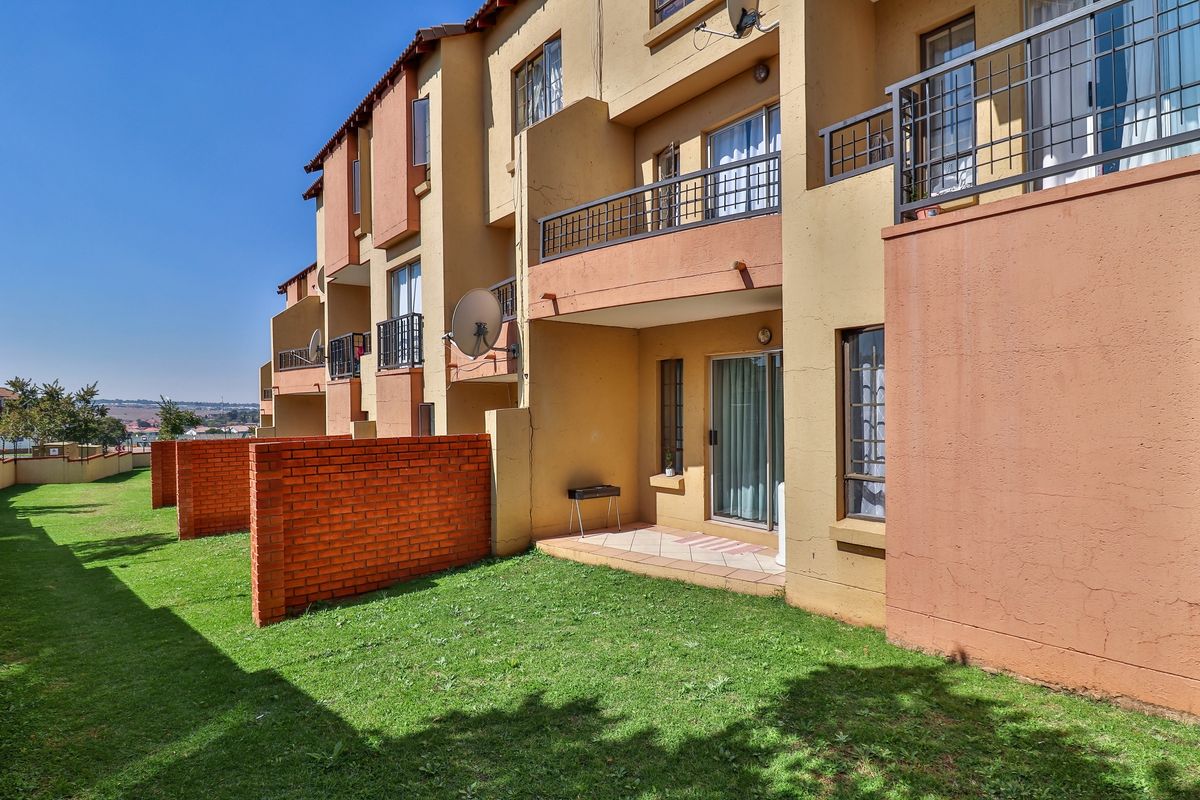 Rear view of the apartment complex featuring ground floor patios with brick privacy walls, sliding door access, and upper-level balconies with metal railings.