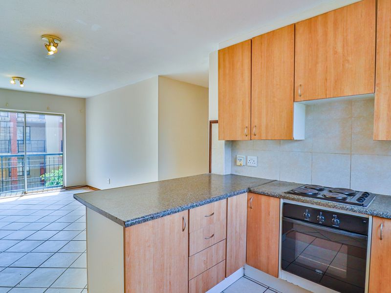 Open-plan kitchen featuring wood-look cabinetry, electric hob, and oven, flowing into a tiled living area with access to a private balcony.