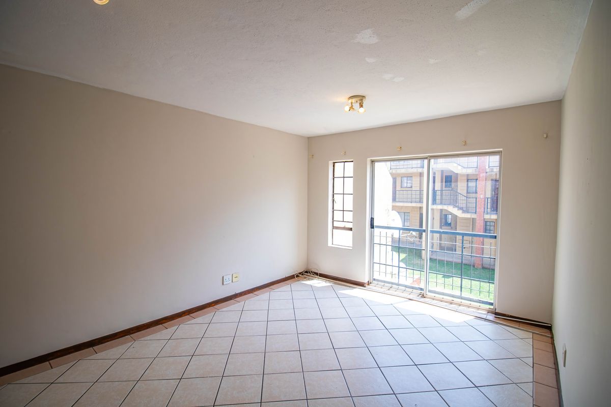An empty, tiled living room featuring a sliding glass door that opens to a balcony, providing natural light and views of the complex.