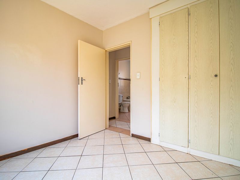 An empty bedroom featuring tiled flooring and built-in cupboards, with an adjoining bathroom visible through the doorway.