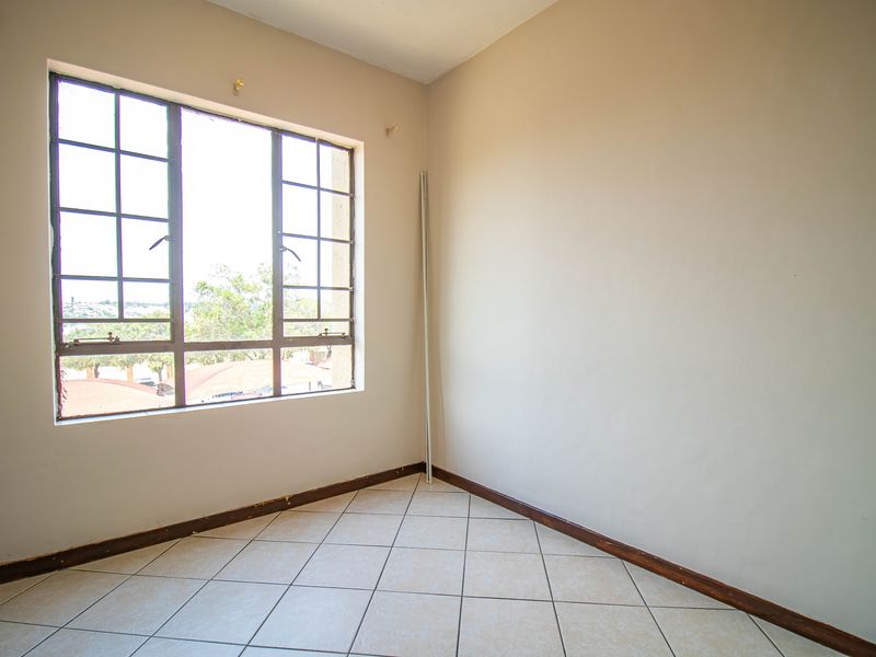 An empty bedroom featuring tiled flooring and a large metal-framed window, offering a blank canvas for personalization.