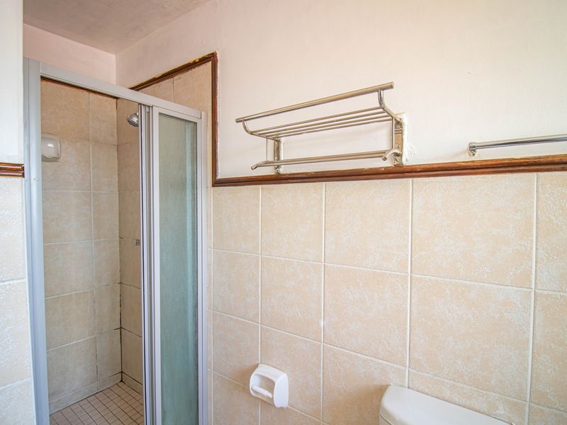 A functional bathroom featuring a shower enclosure with tiled walls and floor, equipped with a wall-mounted towel rack and toilet paper holder.
